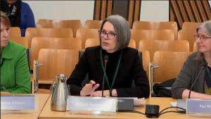 Alison Bavidge sitting at a table and speaking.